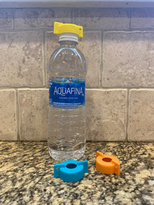 Yellow cap with wings sitting on top of the cap of an Aquafina water bottle. Two additional winged lids in blue and orange sit on the marble countertop.