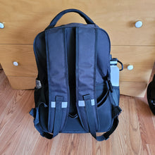 Load image into Gallery viewer, View of the bag from the back. Two &quot;shoulder&quot; straps (like a backpack) are visible, each with a small reflector strip across the middle of the strap. The handle is clearly visible on top.

