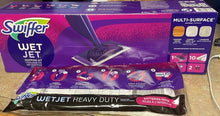 Load image into Gallery viewer, The Swiffer WetJet Mult-Surface in its packaging, a purple box with an image of the mop head and then a package on the floor beside it, which depicts step-by-step instructions for setting it up.
