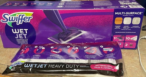 The Swiffer WetJet Mult-Surface in its packaging, a purple box with an image of the mop head and then a package on the floor beside it, which depicts step-by-step instructions for setting it up.