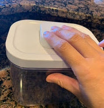 Load image into Gallery viewer, Pop container, clear with a white lid, sitting on a marble countertop. An adult hand is pushing the button on the lid.
