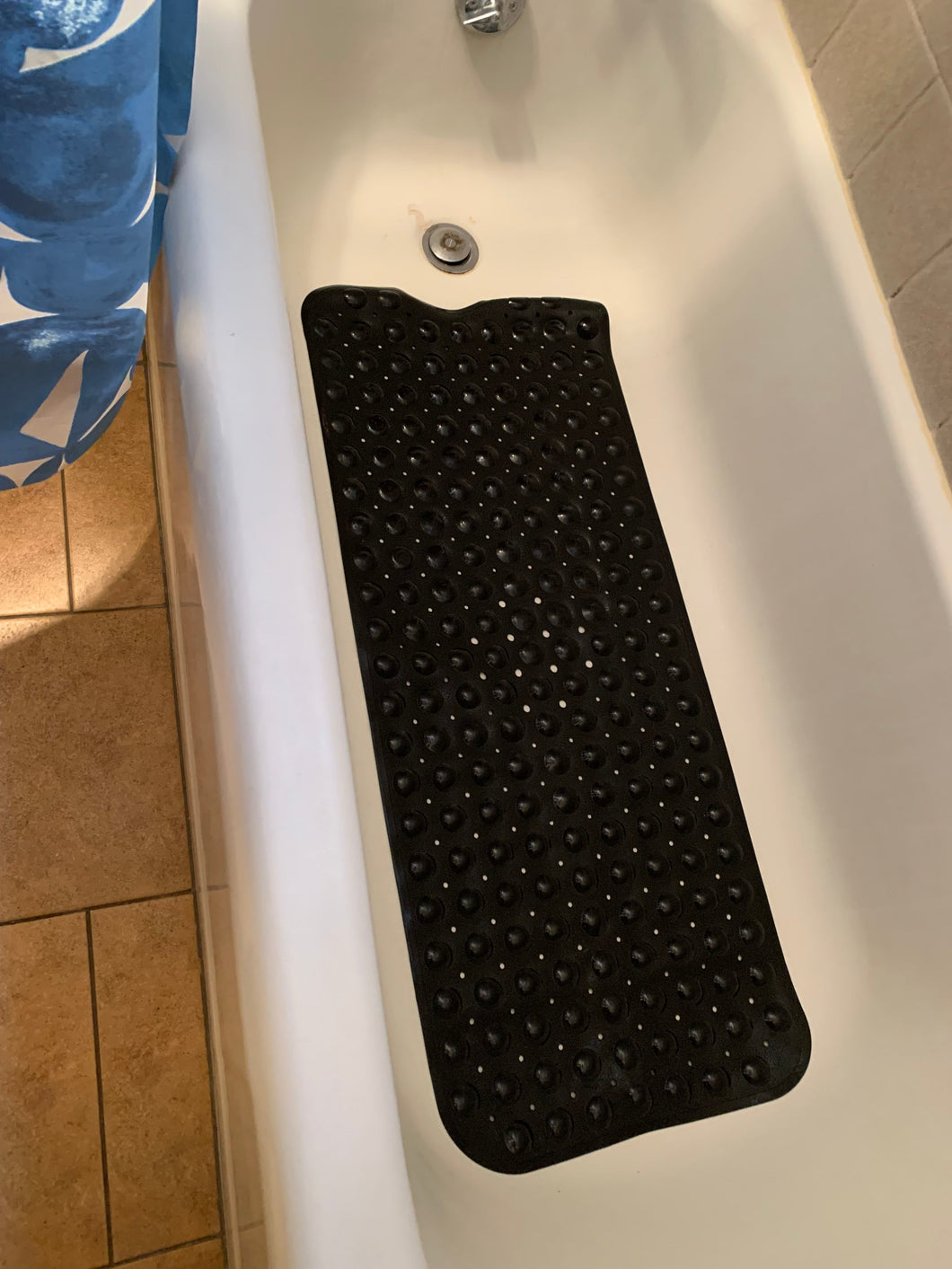 A long black shower mat with small holes is on the floor of a white bathtub.