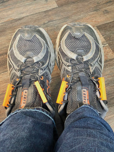 Top-down photo of black athletic sneakers with orange Zubits magnetic shoelaces that are open.